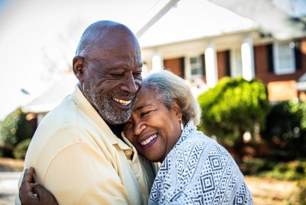 Elderly couple hugging in front of their house