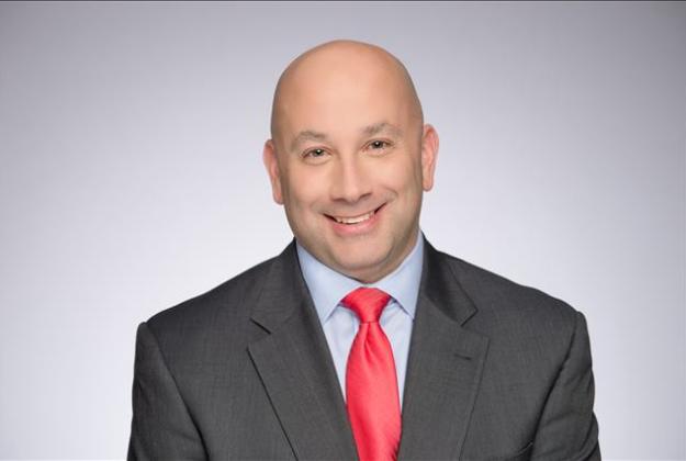 Ryan Hanna wears a black suit jacket, red tie, and smiles at the camera