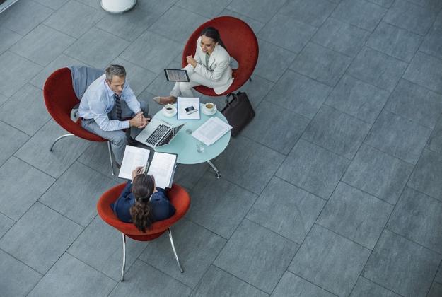 Three colleagues gather at a small coffee table to discuss finances