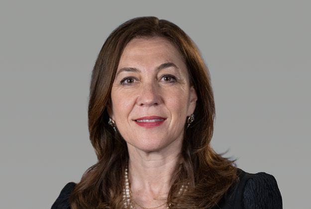 Eva wears a black top, has long brown hair, and smiles at the camera