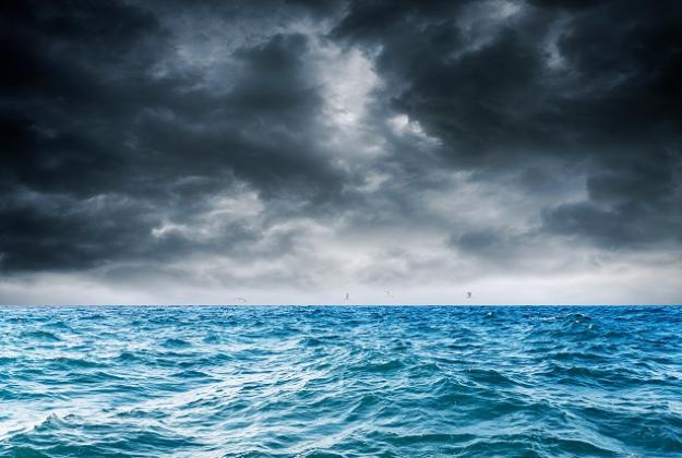 A turbulent ocean swells beneath a dark ominous sky