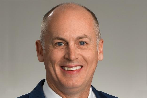 Scott Tuxbury wears a suit and smiles at the camera