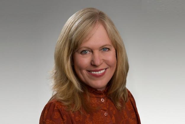 Diana wears a red sweater, has shoulder-length blonde hair, and smiles at the camera