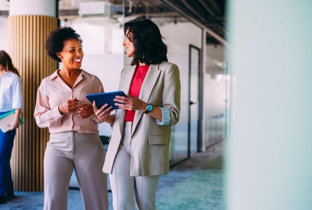 Two women have a conversation as they walk together through an office