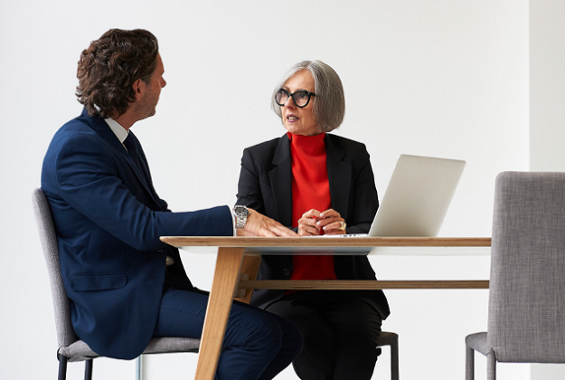 A relationship manager sits with a client at a table to review financials on a laptop