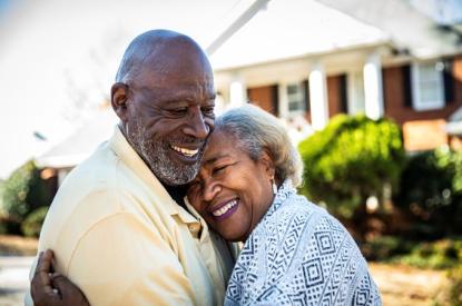 Elderly couple hugging in front of their house