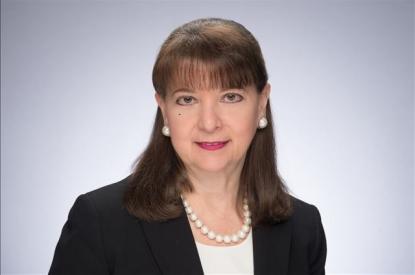 Susan Martore-Baker wears a blue suit jacket, pearl necklace and earrings, and smiles at the camera