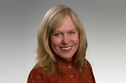 Diana wears a red sweater, has shoulder-length blonde hair, and smiles at the camera