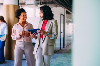 Two women have a conversation as they walk together through an office