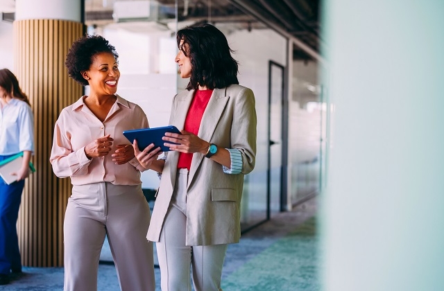 Two women have a conversation as they walk together through an office